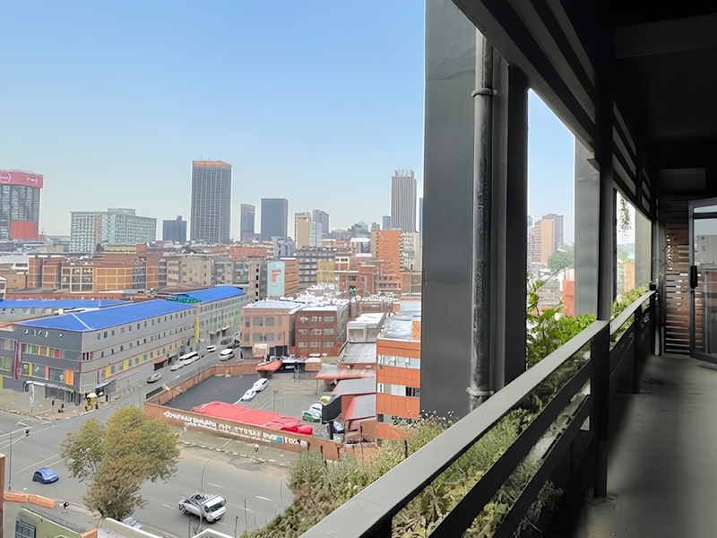 A covered balcony area featuring a metal railing and sliding door access, offering an expansive elevated view of the surrounding city skyline.