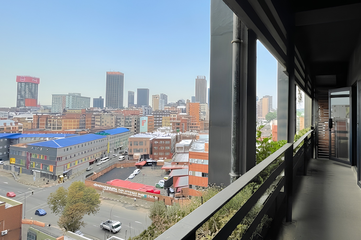 A covered balcony area featuring a metal railing and sliding door access, offering an expansive elevated view of the surrounding city skyline.