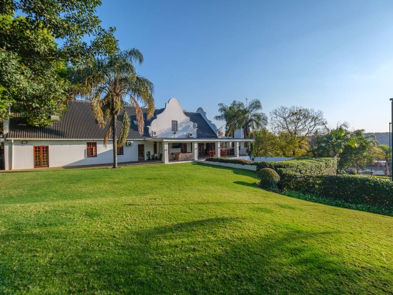 Spacious rear garden view featuring a well-maintained lawn, landscaped hedges, and a covered patio area attached to the main residence.