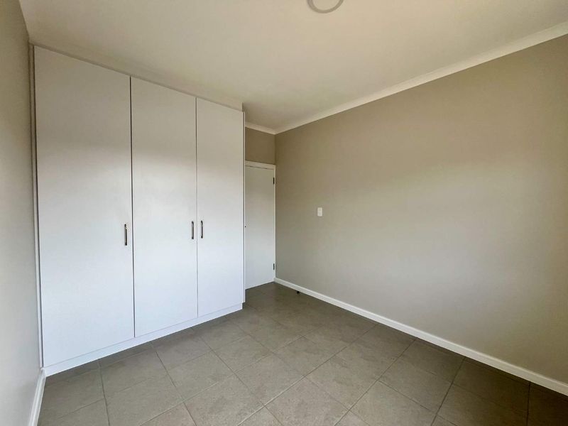 A clean, empty bedroom featuring neutral wall tones, tiled flooring, and ample built-in cupboard storage.