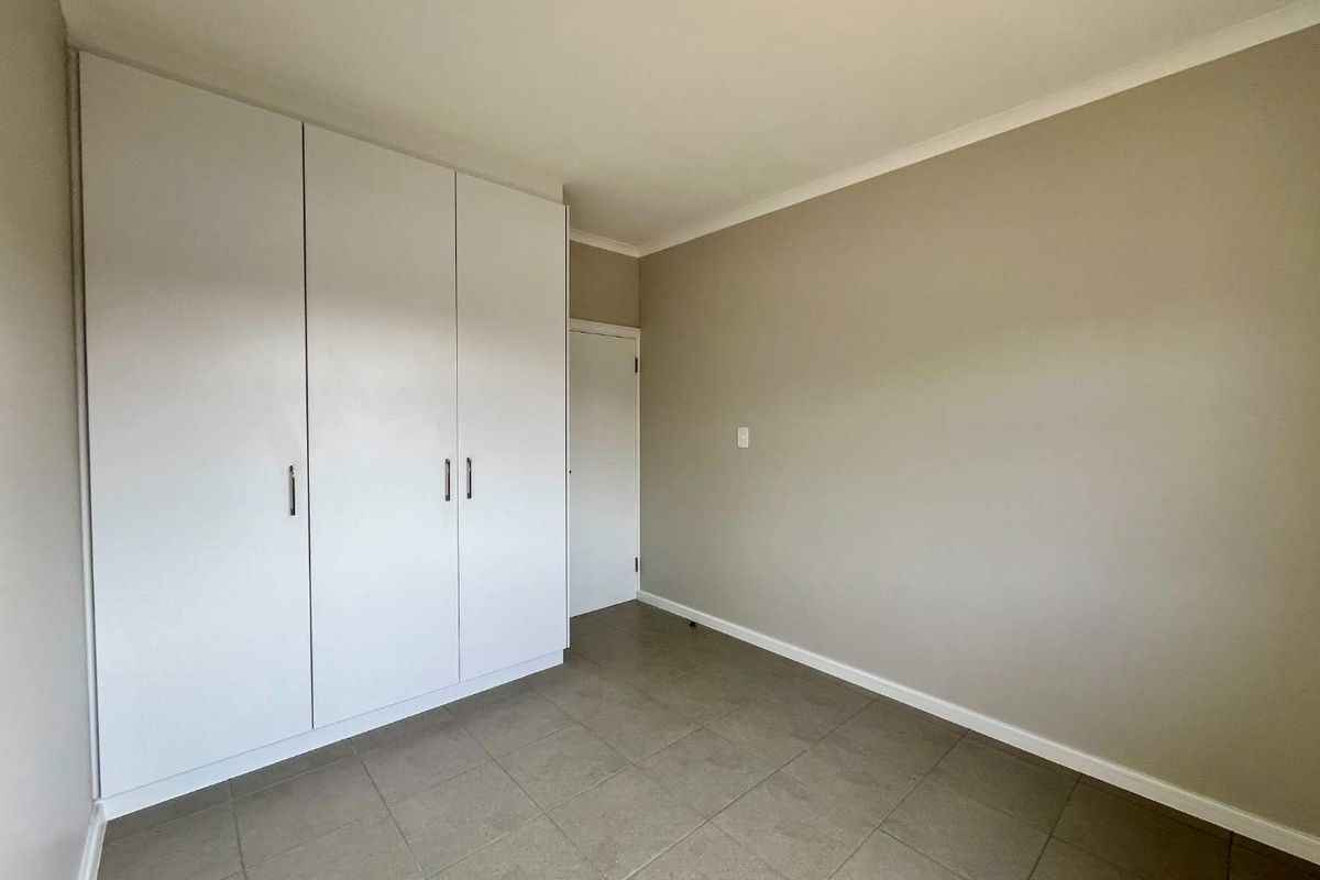 A clean, empty bedroom featuring neutral wall tones, tiled flooring, and ample built-in cupboard storage.