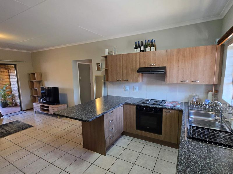 Open-plan living area featuring a functional kitchen with laminate cabinetry, granite countertops, built-in oven, hob, and a breakfast nook, flowing onto a covered patio.