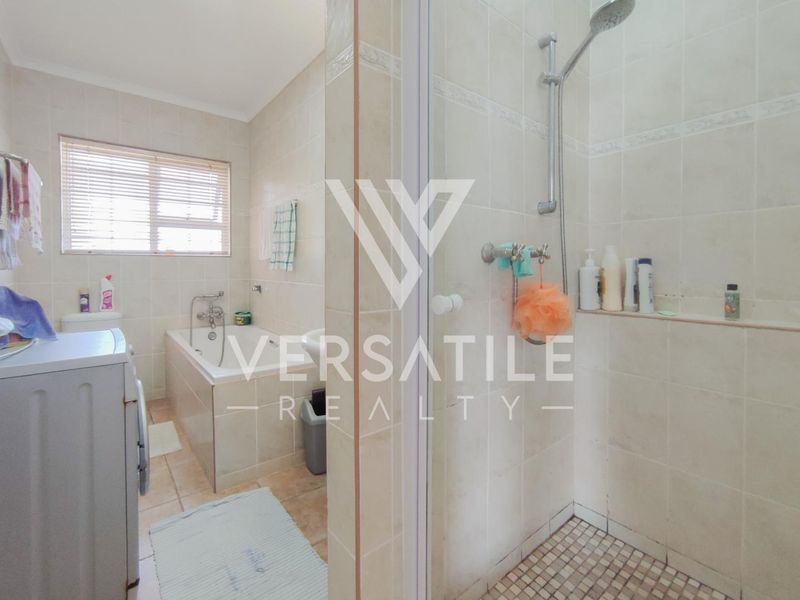 A functional bathroom featuring a built-in bathtub, separate shower enclosure, and neutral wall tiling throughout.