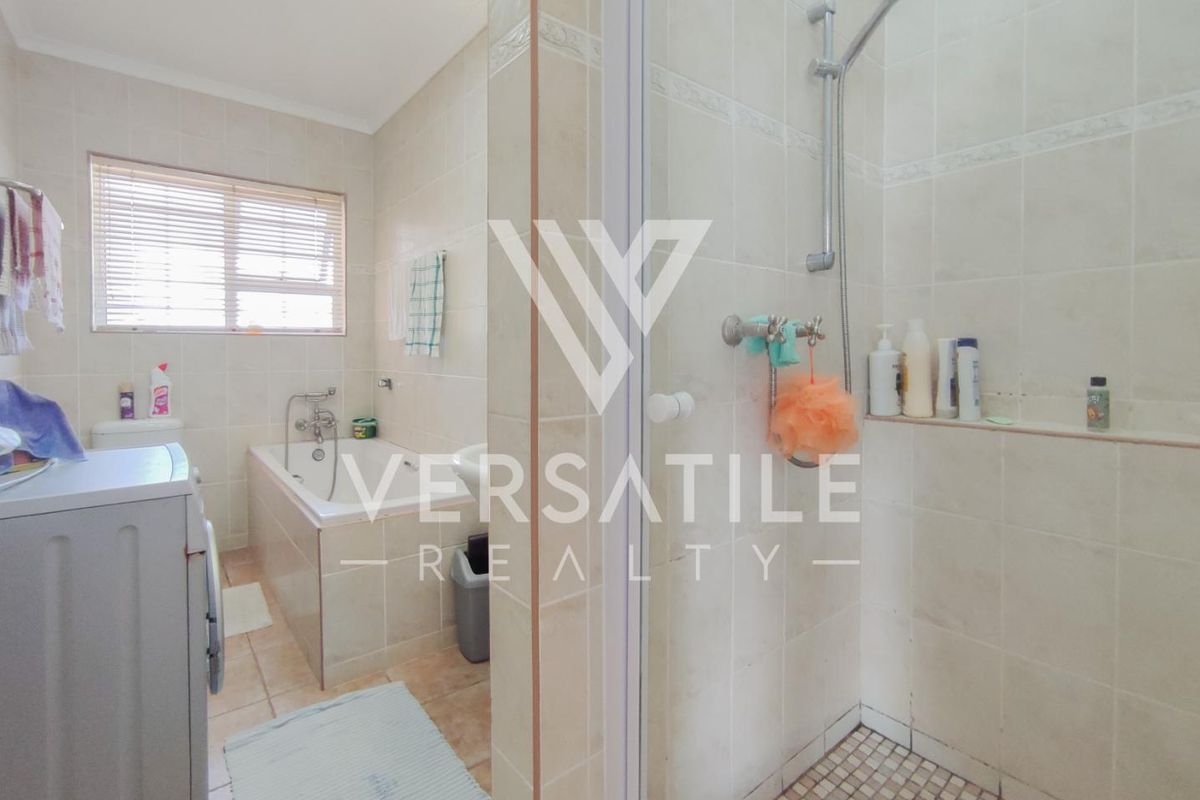 A functional bathroom featuring a built-in bathtub, separate shower enclosure, and neutral wall tiling throughout.
