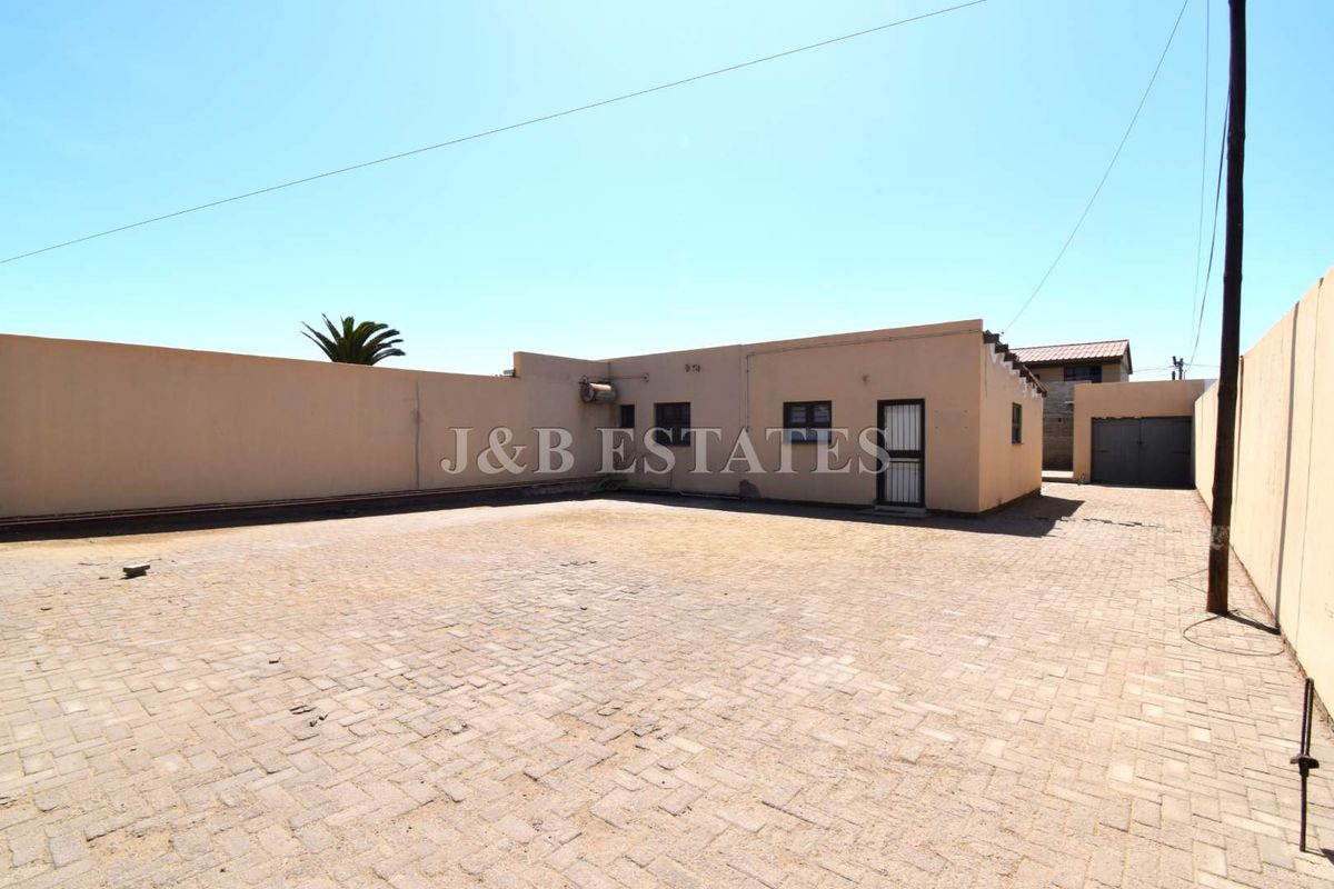A spacious paved rear courtyard area featuring high perimeter boundary walls and access to the main building structure.