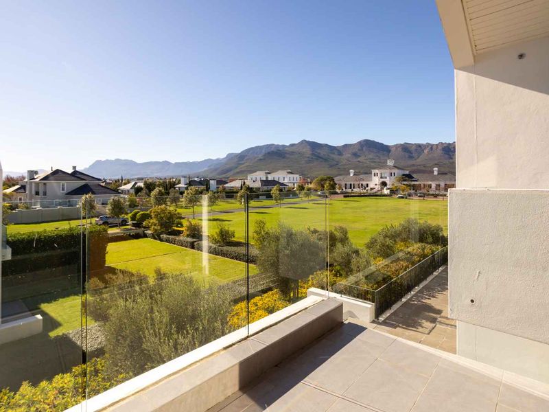 A spacious balcony featuring a modern glass balustrade and tiled flooring, offering expansive views of the surrounding estate and mountain range.