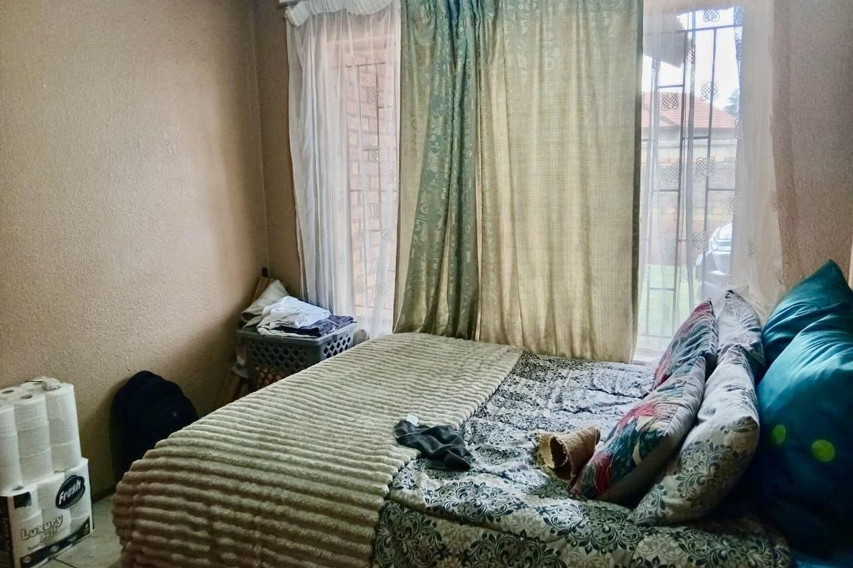 A bedroom featuring a large window with security bars and neutral wall finishes, providing a functional sleeping space.