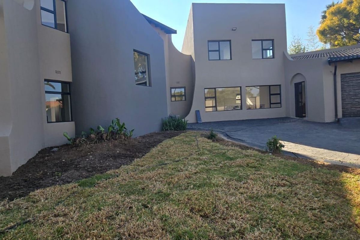 Rear view of the property featuring a paved driveway, double garage, and established garden area with modern architectural lines.