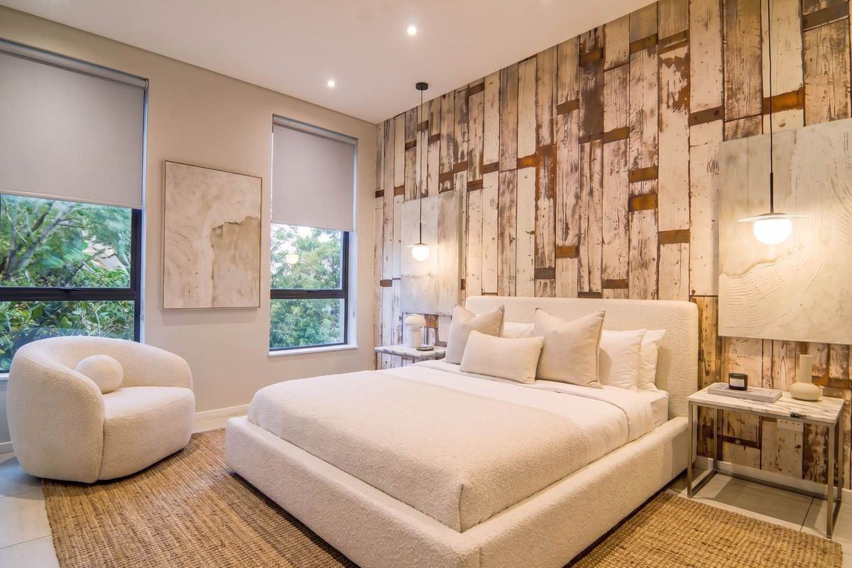 A well-appointed bedroom featuring a textured wood-look feature wall, recessed downlighting, and large windows with roller blinds, creating a bright and modern atmosphere.