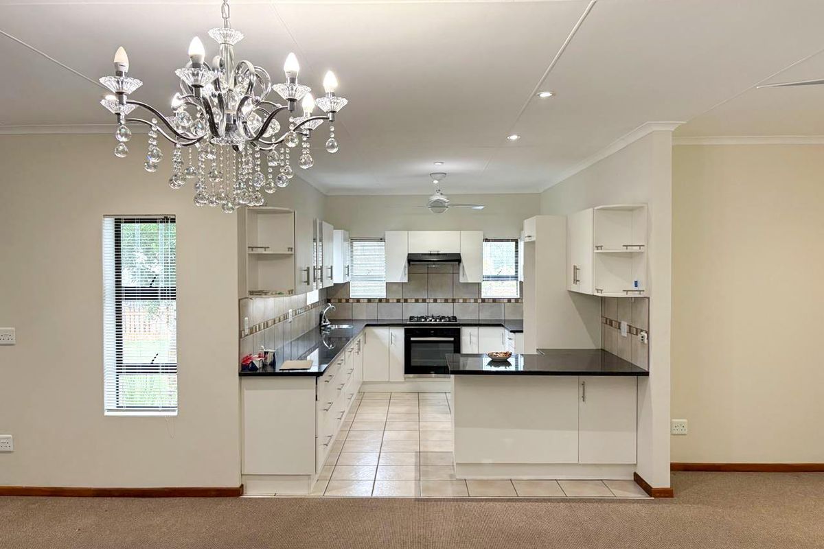 A functional kitchen featuring white cabinetry, dark countertops, a built-in oven, and a gas hob, seamlessly integrated into an open-plan living space.