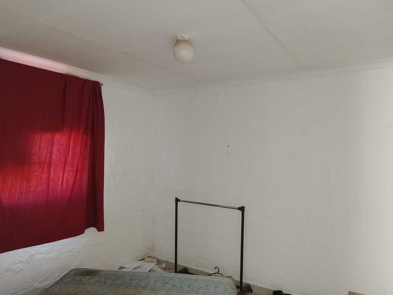 A basic bedroom space featuring plain white walls and a simple ceiling light fixture, requiring cosmetic updates and repairs to the wall finishes.