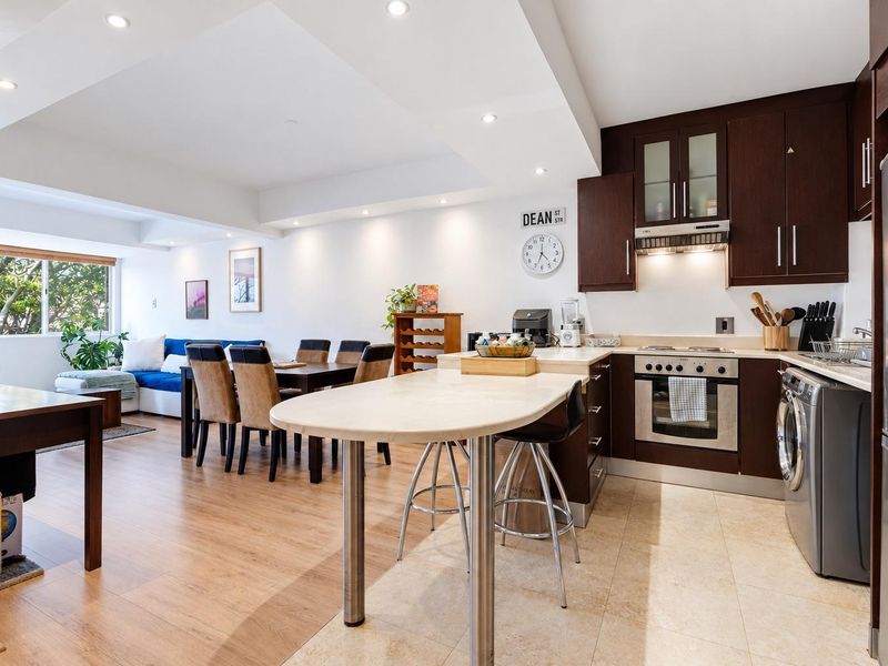 Open-plan living and dining area featuring a modern kitchen with dark wood cabinetry, stone countertops, integrated appliances, and recessed lighting.