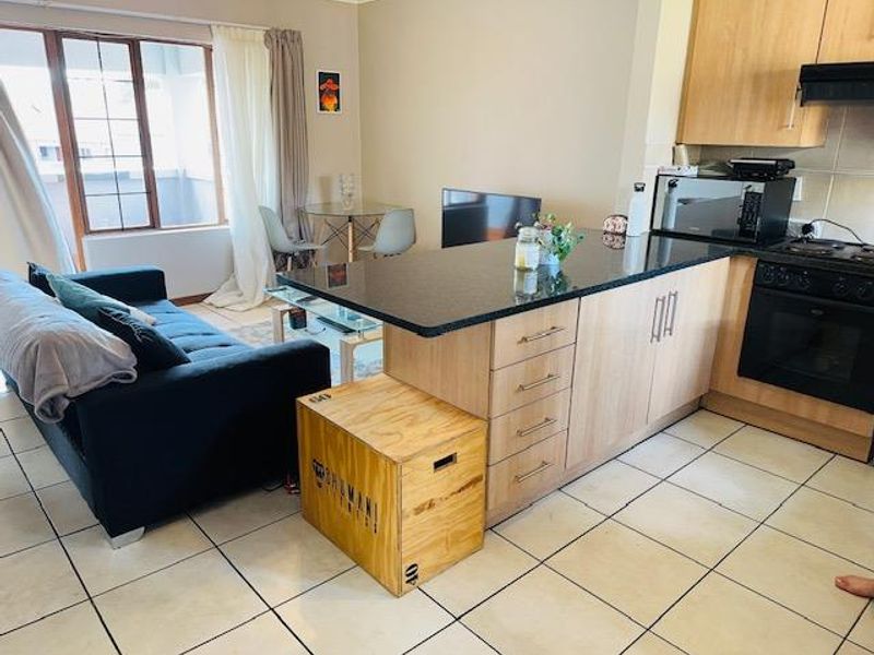 Open-plan living area featuring a kitchen with granite island, built-in oven, gas hob, and tiled flooring, seamlessly connecting to the lounge space.
