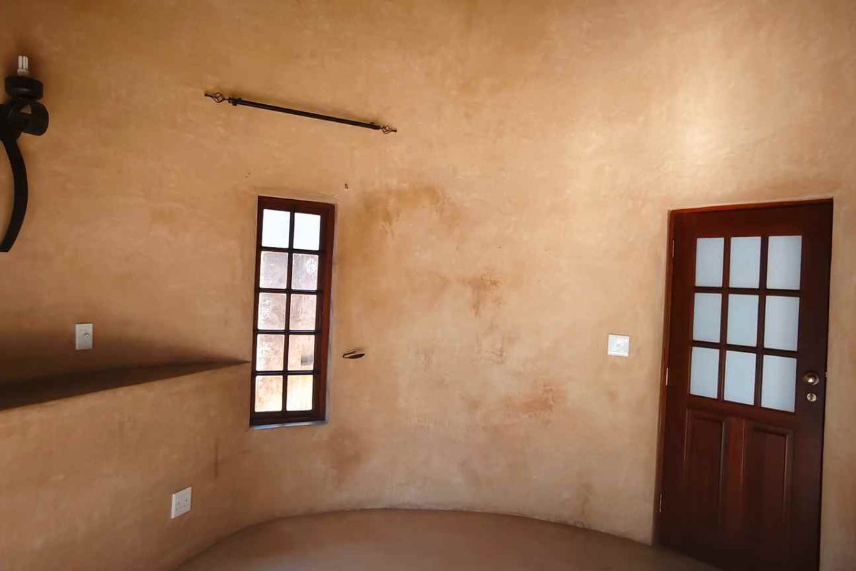 A unique circular room featuring rustic textured walls, a timber-framed window, and a classic wooden door with glass panes.