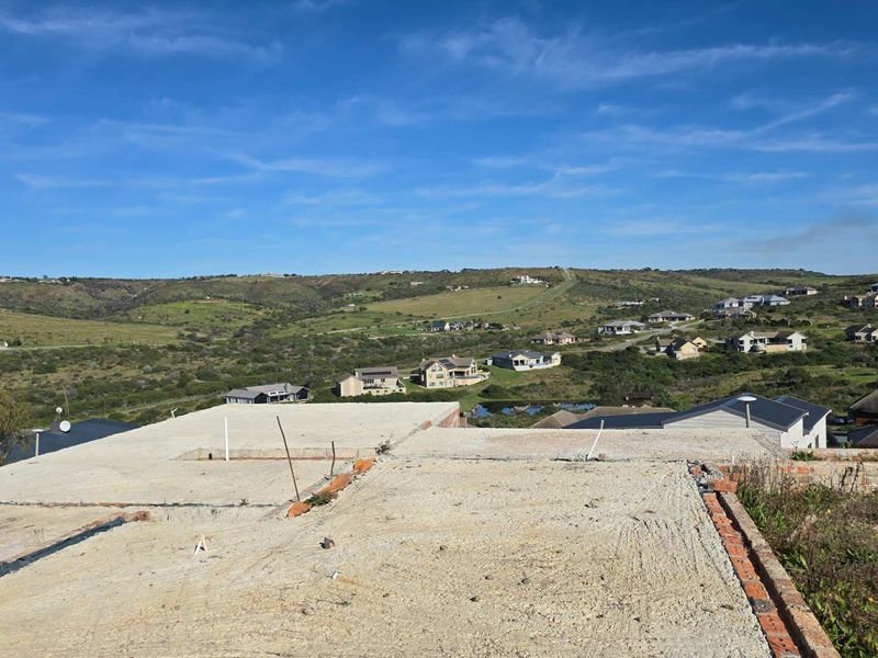 An elevated view of a property under construction, featuring an exposed concrete slab foundation and brickwork with expansive views of the surrounding landscape.