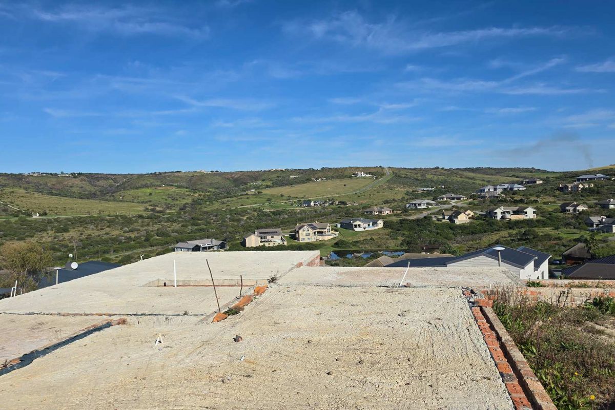 An elevated view of a property under construction, featuring an exposed concrete slab foundation and brickwork with expansive views of the surrounding landscape.