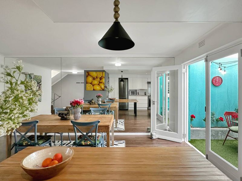 Bright open-plan living and dining area featuring modern kitchen cabinetry, mirrored wall accents, and direct access to a private outdoor courtyard through french doors.
