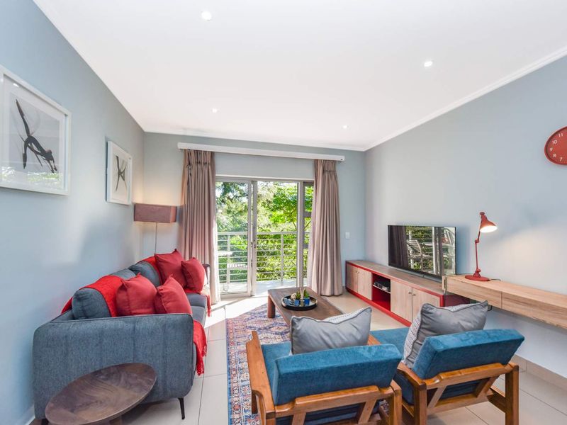 A bright and well-maintained living room featuring tiled flooring, recessed lighting, and a sliding glass door providing access to a balcony.