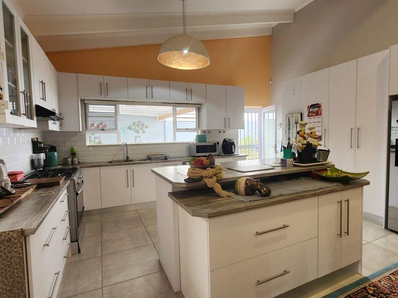 A well-lit, modern kitchen featuring white cabinetry, a central island with a wood-look countertop, subway tile backsplash, and a vaulted ceiling.