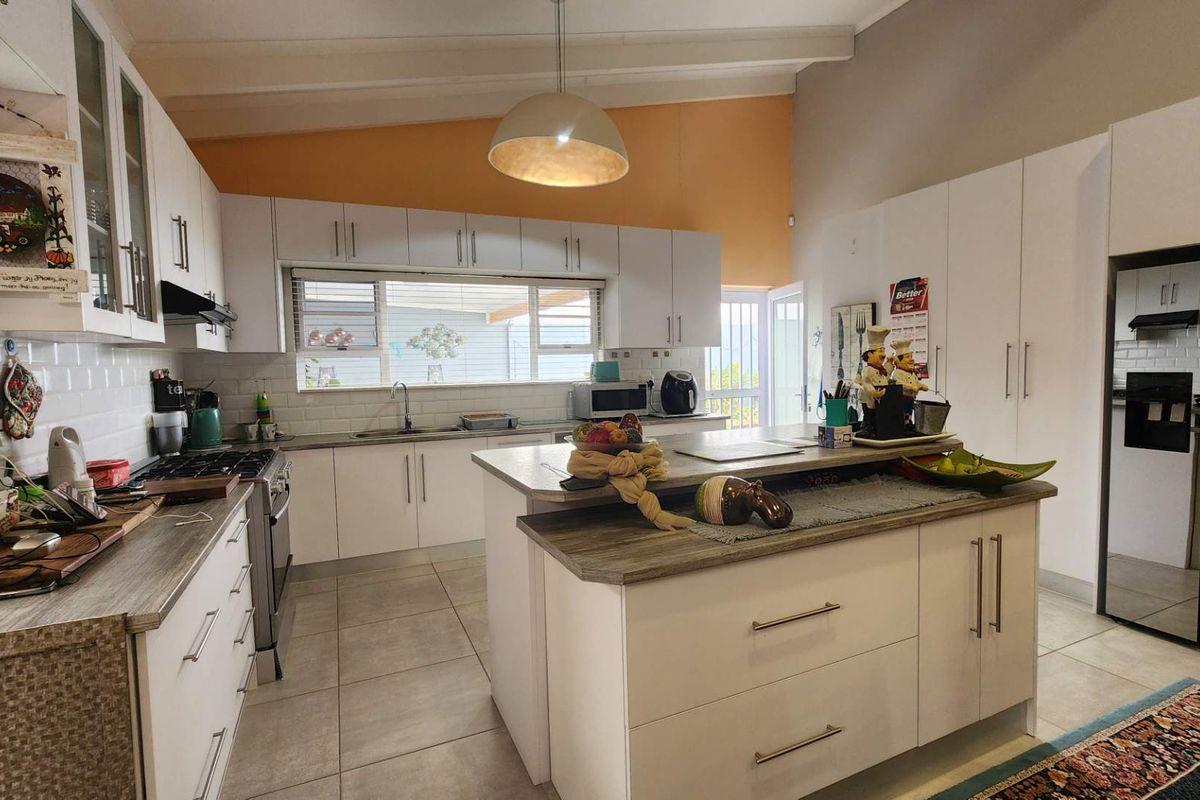 A well-lit, modern kitchen featuring white cabinetry, a central island with a wood-look countertop, subway tile backsplash, and a vaulted ceiling.