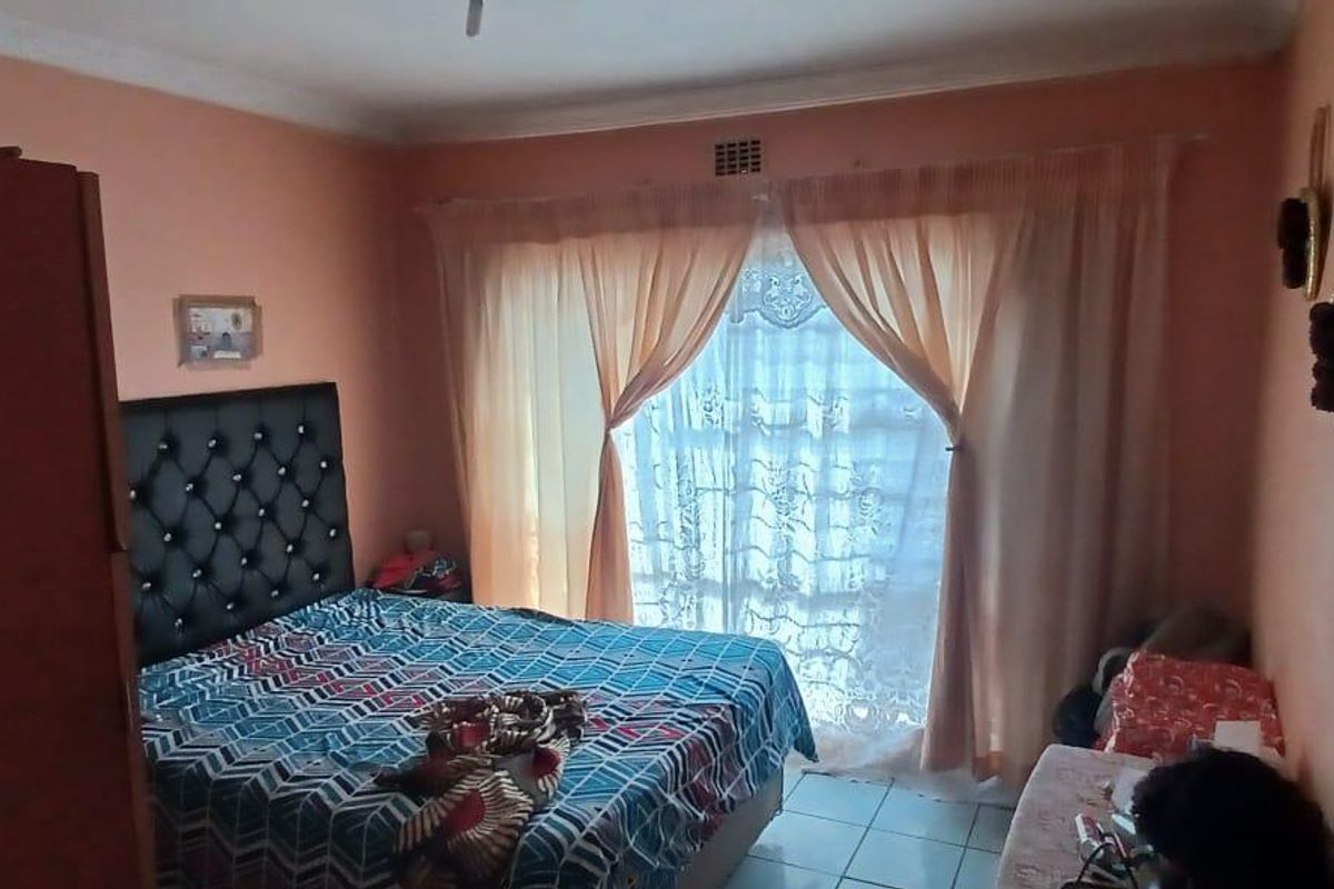 A bedroom featuring tiled flooring, a large window with curtaining, and neutral wall tones, offering a functional space for rest.