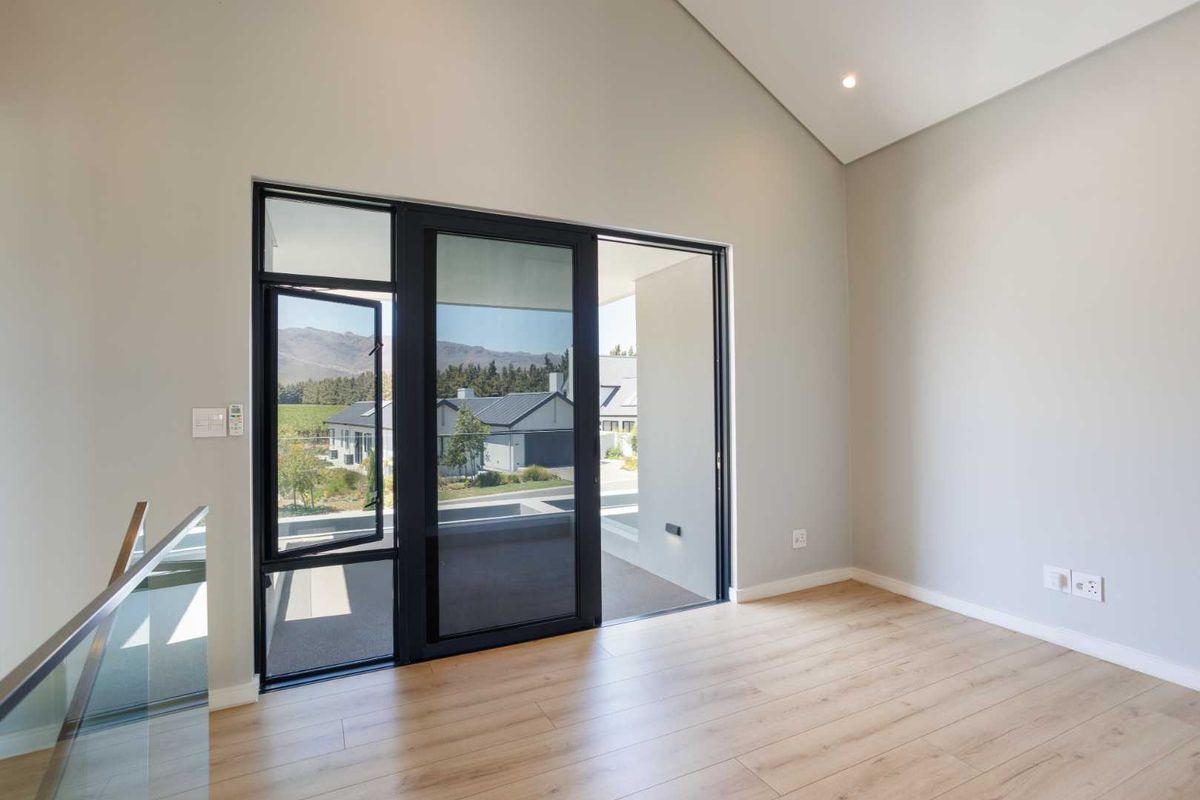 A bright, modern living space featuring high vaulted ceilings, light wood-look flooring, and large black-framed glass doors opening to an outdoor area.