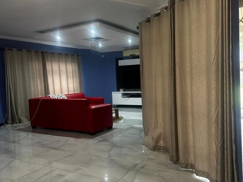 Spacious living room featuring polished porcelain floor tiles, a modern recessed ceiling with cove lighting, and an integrated air conditioning unit.