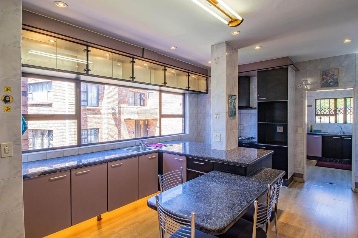 A well-lit kitchen featuring granite countertops, built-in cabinetry, recessed lighting, and a breakfast nook, with an adjacent scullery area visible.