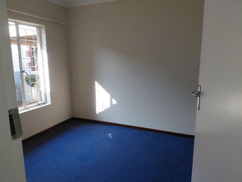 An empty bedroom featuring blue carpeting, neutral walls, and a window fitted with security bars.