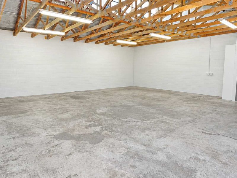 Spacious industrial utility area featuring exposed timber roof trusses, durable concrete flooring, painted blockwork walls, and secure gated access.