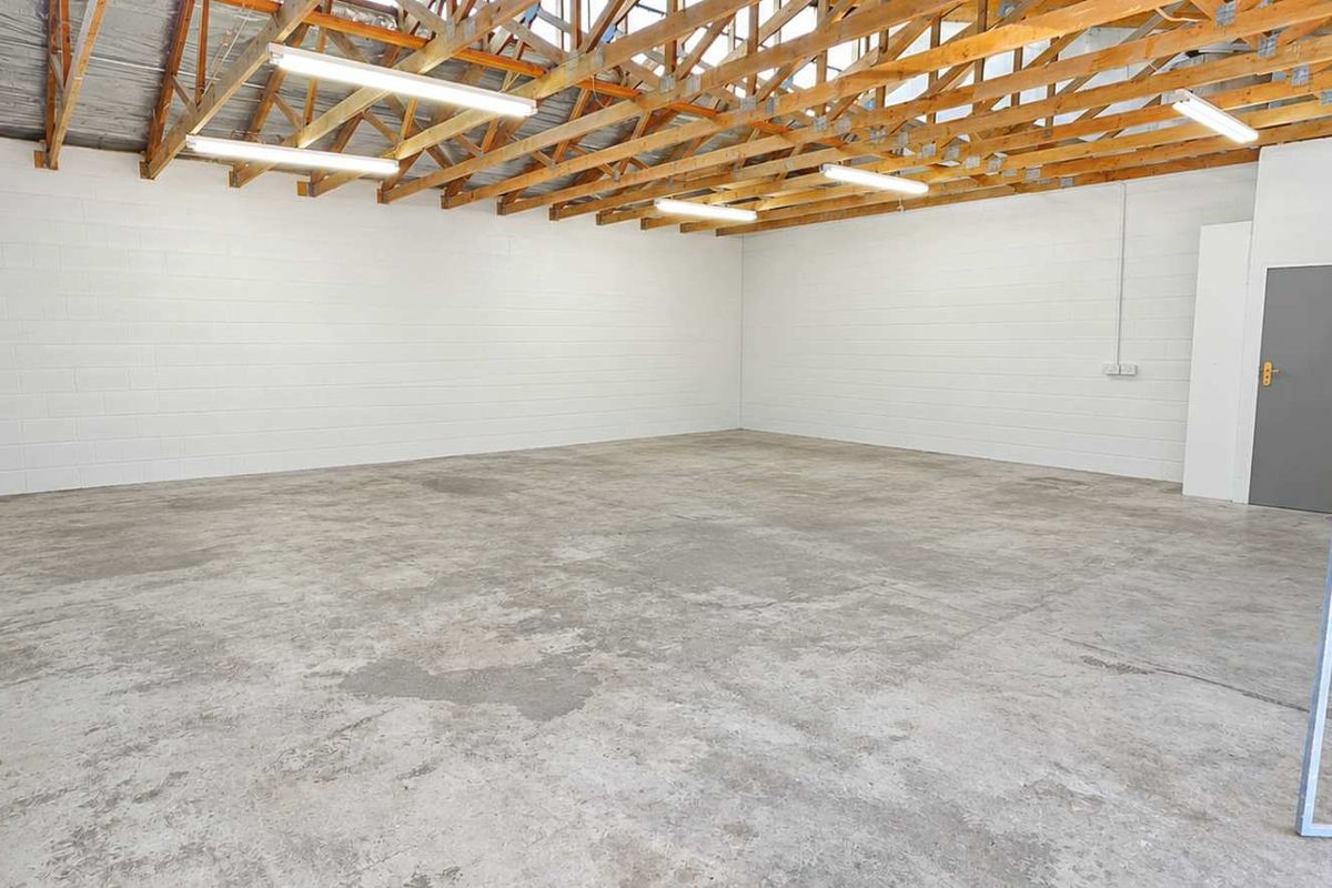 Spacious industrial utility area featuring exposed timber roof trusses, durable concrete flooring, painted blockwork walls, and secure gated access.
