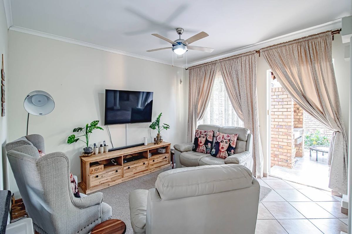 A bright living room featuring tiled flooring, a ceiling fan, and direct access to an outdoor patio area through a glass door.