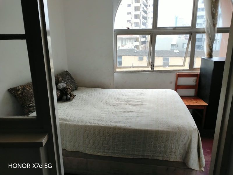 A bedroom featuring an arched window with city views, requiring cosmetic updates to the wall finishes.