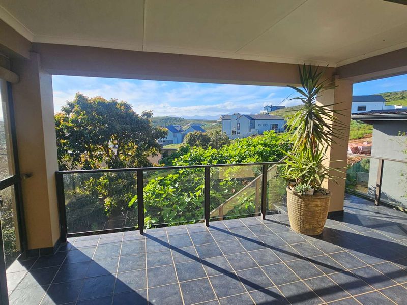 A spacious covered balcony featuring dark tiled flooring and a modern glass balustrade, offering pleasant views of the surrounding neighbourhood.
