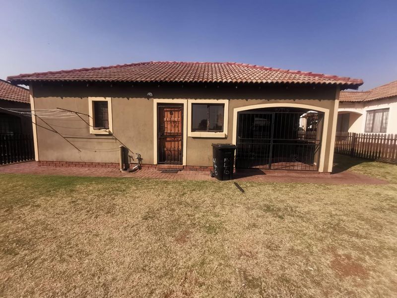 Rear view of the cluster home featuring a tiled roof, paved walkway, and a private garden area with perimeter fencing.