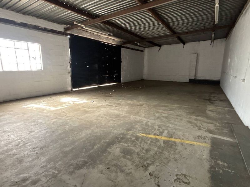 Spacious industrial garage or warehouse unit featuring concrete flooring, a high corrugated metal ceiling, and a large roller shutter door.