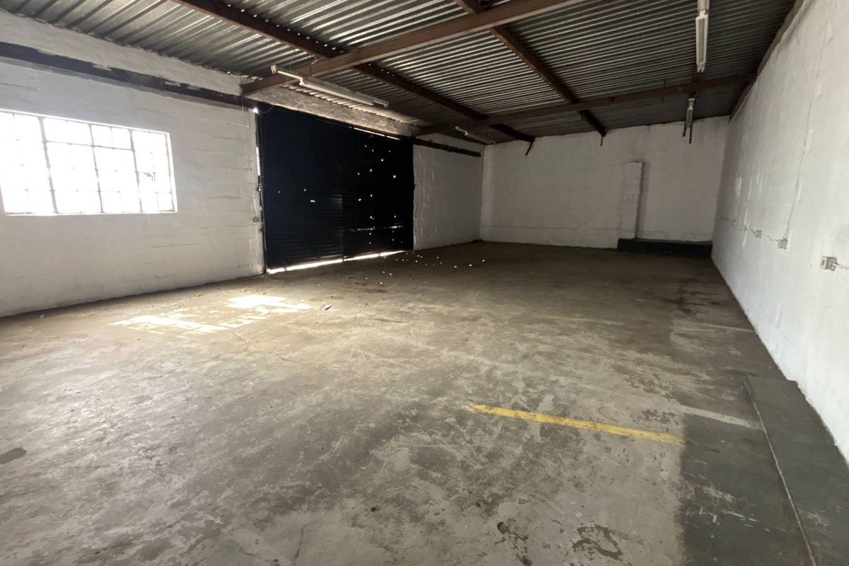 Spacious industrial garage or warehouse unit featuring concrete flooring, a high corrugated metal ceiling, and a large roller shutter door.