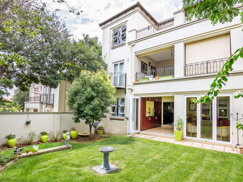Rear view of a multi-story apartment building featuring a private garden, ground floor patio, and upper-level balconies with wrought iron railings.