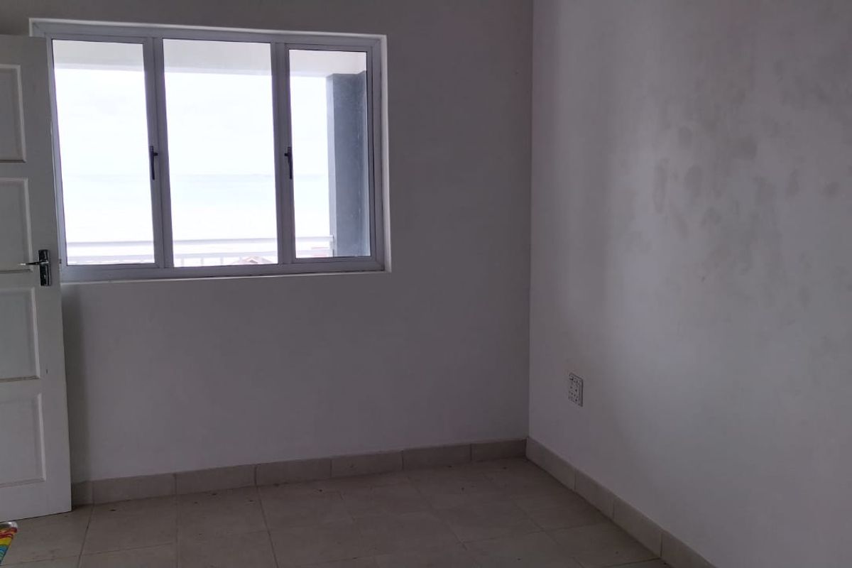 An empty bedroom featuring tiled flooring, a white panel door, and a window with natural light.