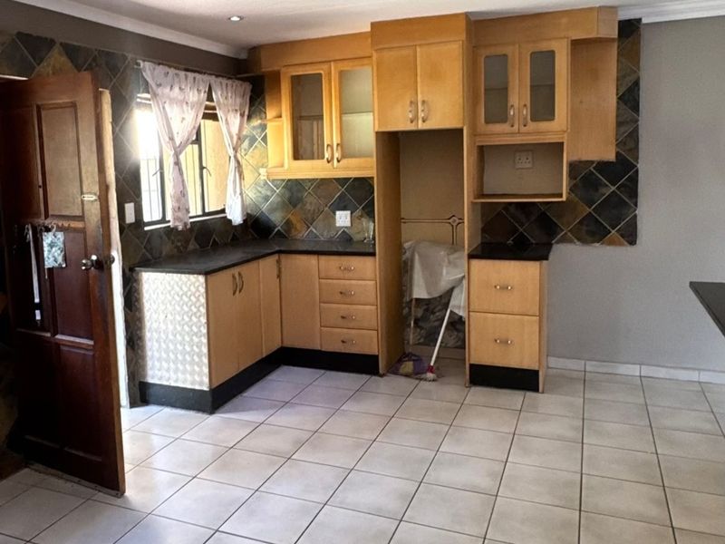 A functional kitchen featuring wooden cabinetry, dark laminate countertops, and tiled flooring, offering a practical layout with potential for modern cosmetic updates.