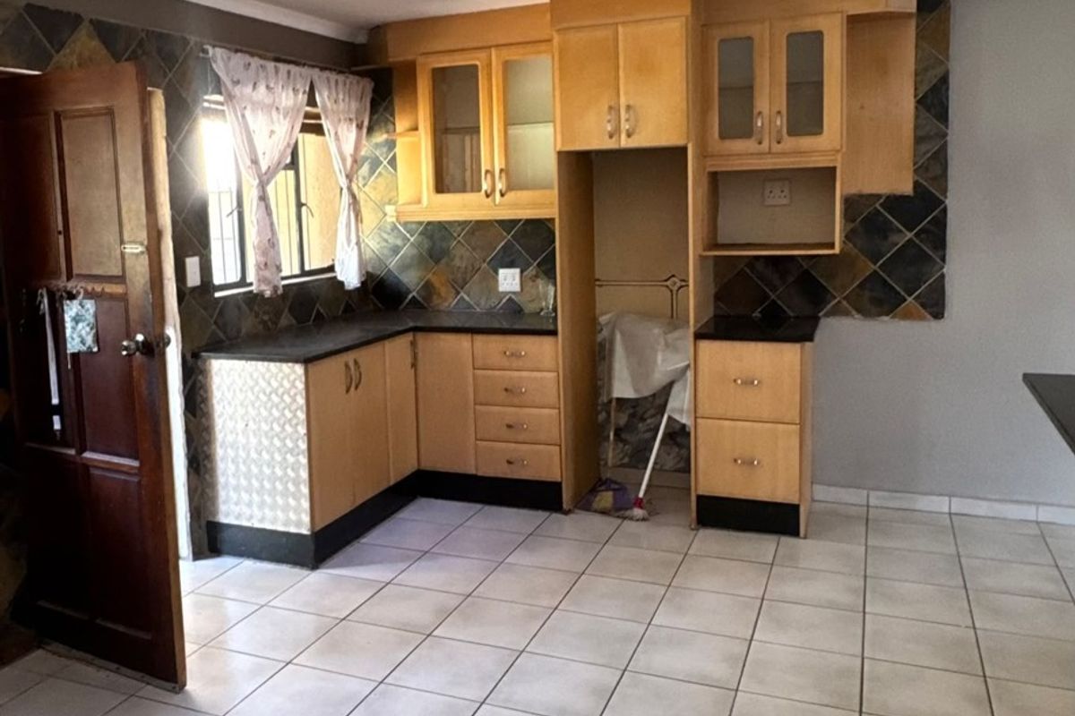 A functional kitchen featuring wooden cabinetry, dark laminate countertops, and tiled flooring, offering a practical layout with potential for modern cosmetic updates.