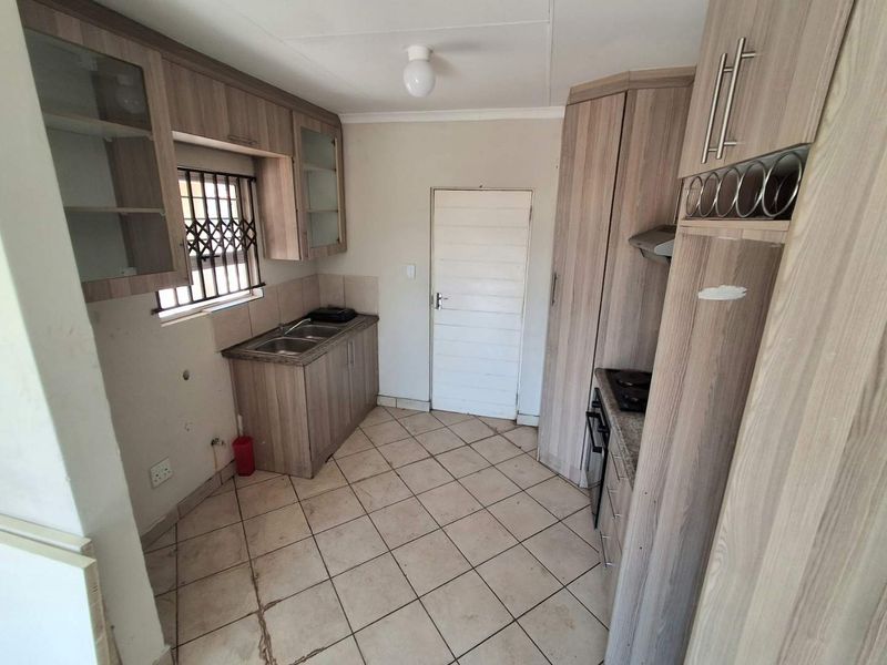 A functional kitchen featuring laminate cabinetry, built-in oven, hob, extractor fan, and tiled flooring, currently vacant and ready for updates.