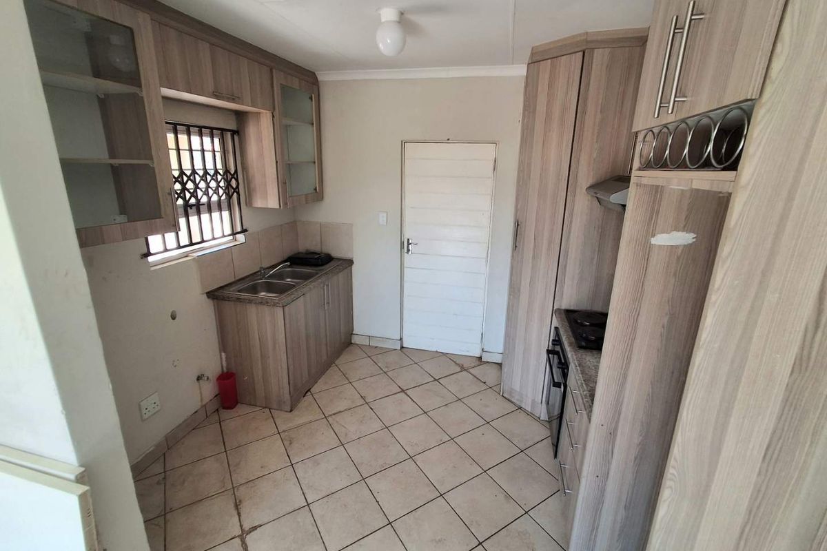 A functional kitchen featuring laminate cabinetry, built-in oven, hob, extractor fan, and tiled flooring, currently vacant and ready for updates.