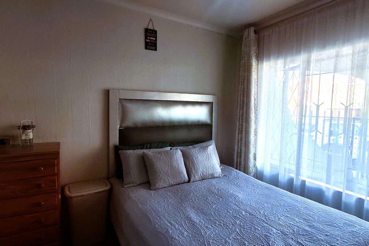 A cozy bedroom featuring natural light through a window fitted with security bars and curtain rails.