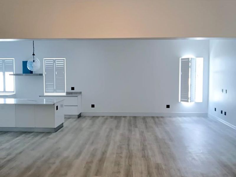 Spacious open-plan living area featuring a modern kitchen island, vaulted ceilings, contemporary pendant lighting, and light-toned laminate flooring throughout.