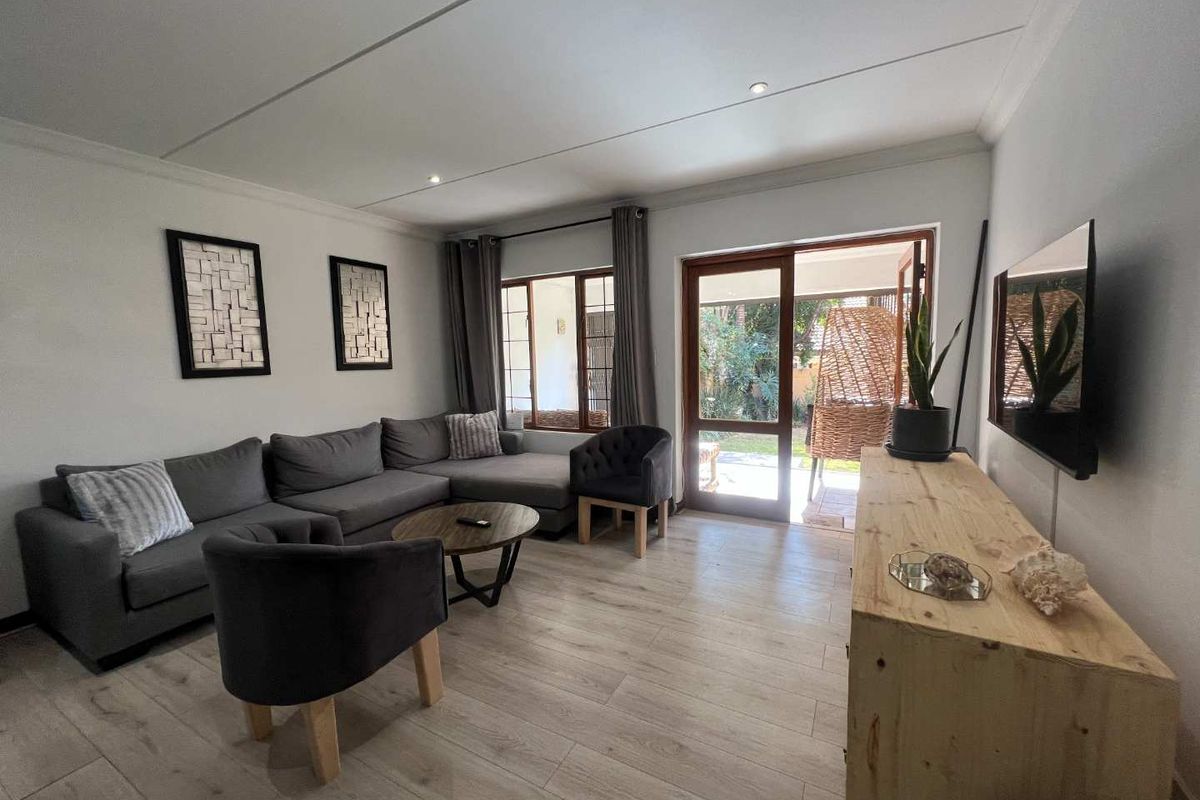 A bright living room featuring light wood-look flooring, recessed ceiling lighting, and direct access to an outdoor patio area through a glass door.