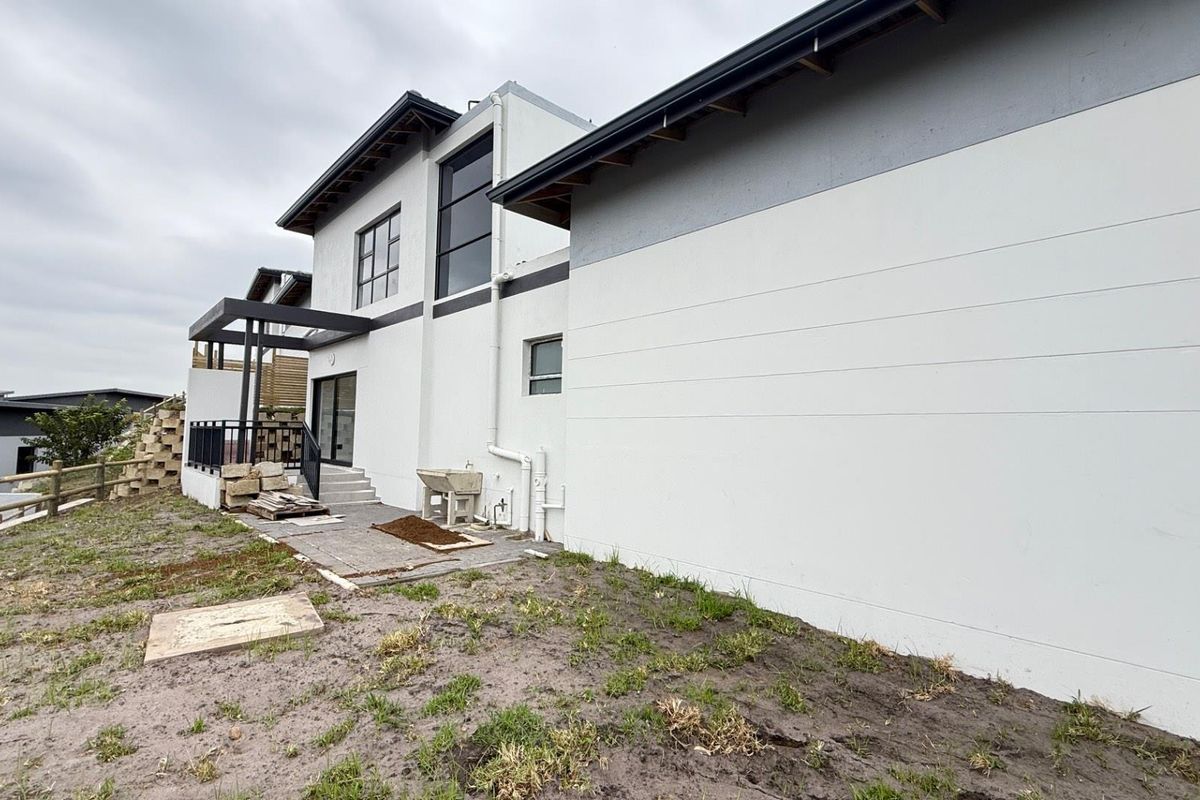 Rear view of the townhouse showing a paved patio area, external plumbing, and unfinished landscaping requiring further development.