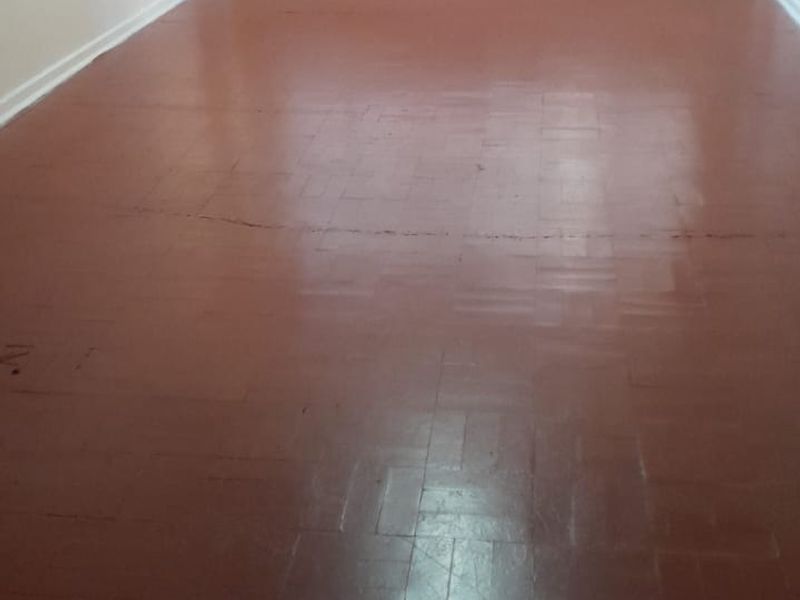 An empty living room featuring original parquet flooring and a large window, providing a blank canvas for renovation and interior design updates.
