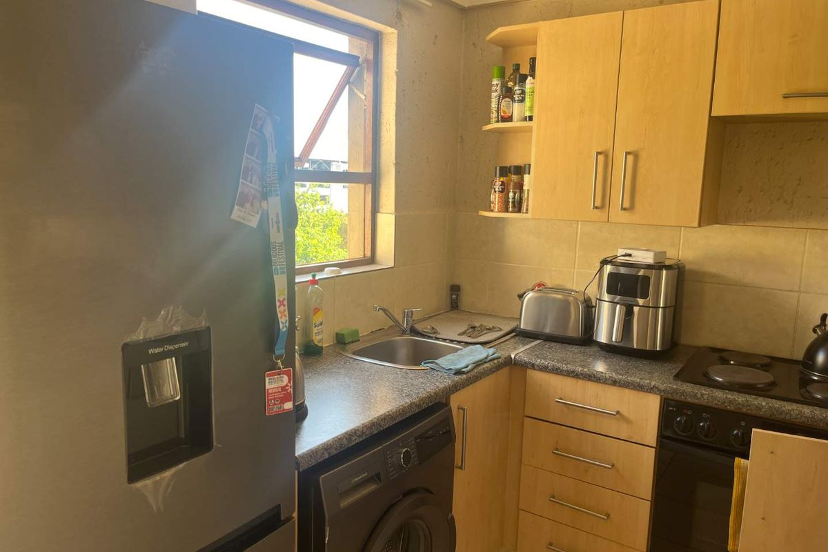 Compact kitchen featuring laminate cabinetry, granite countertops, built-in oven, hob, and integrated laundry plumbing, requiring cosmetic updates to the wall finishes.