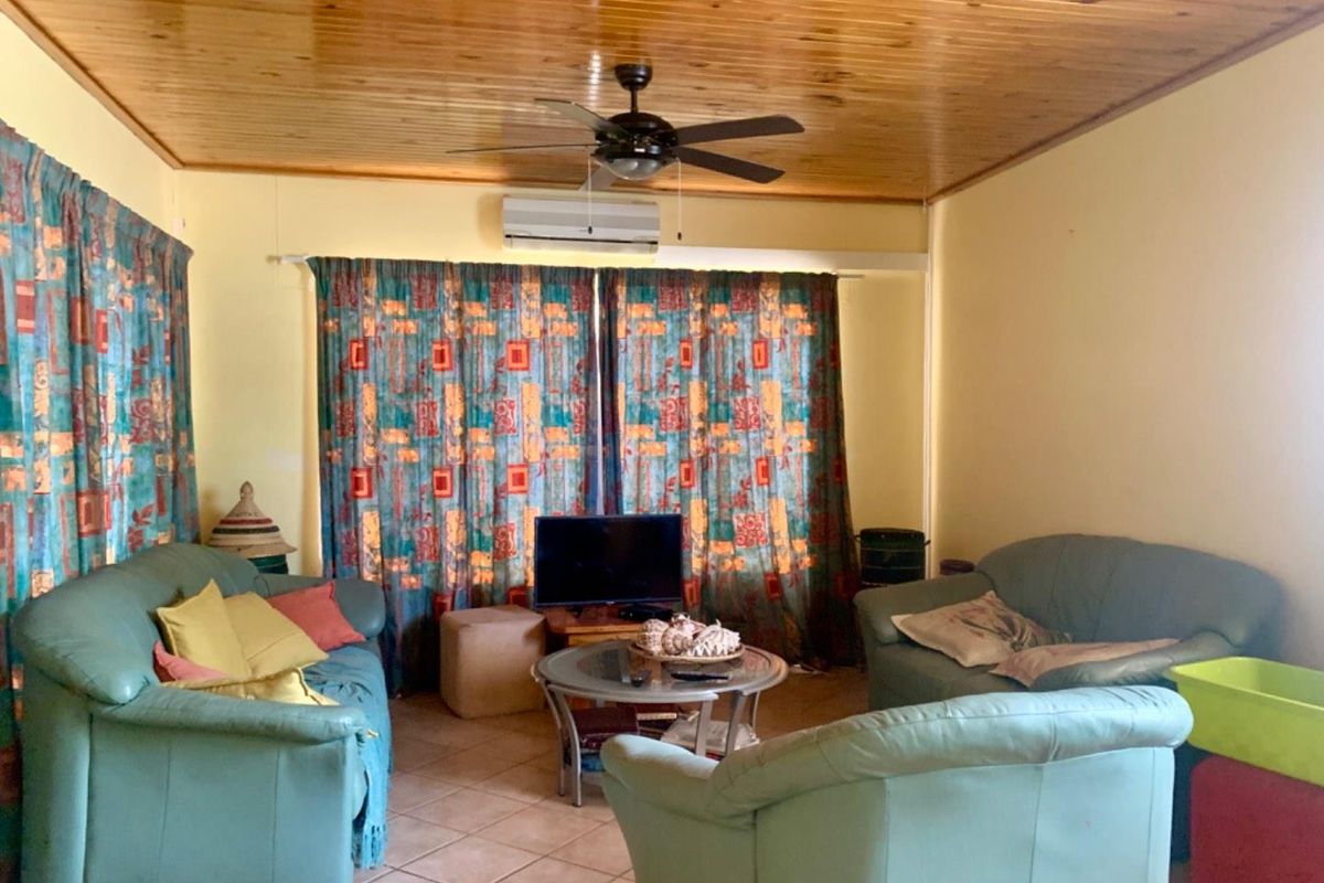 A living room featuring a timber-paneled ceiling, tiled flooring, and a wall-mounted air conditioning unit.